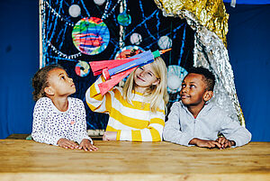 Drei Kinder untersuchen Nachbildungen von Planeten und Raketen