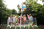 Auf einem umzäunten Podest stehen Kinder mit Luftballons und farbigen Tüchern