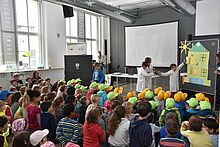 Kinder sitzen in einer Aula hören einer Erklärung zu