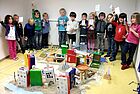 Ein Gruppe Kinder steht um eine Menge gebastelter Häuser in der Mitte des Raumes